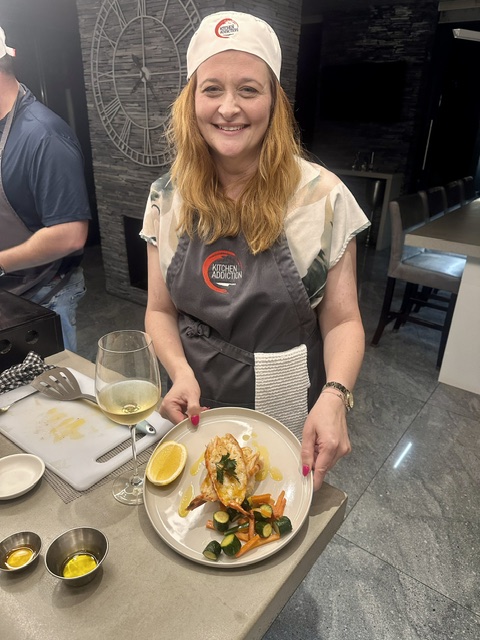 A guest in the Kitchen Addiction kitchen holding the dish she cooked